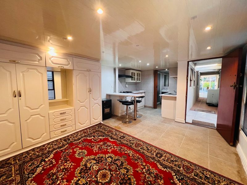 Open-plan living area featuring built-in cabinetry, a compact kitchenette with hob and extractor, recessed lighting, and tiled flooring throughout.
