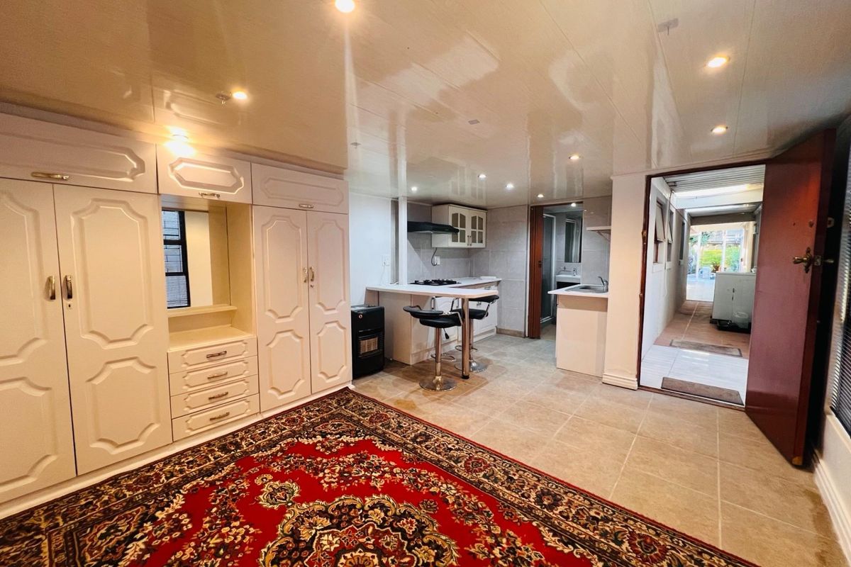 Open-plan living area featuring built-in cabinetry, a compact kitchenette with hob and extractor, recessed lighting, and tiled flooring throughout.