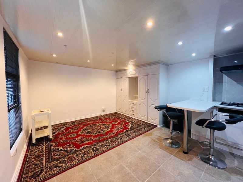 Open-plan living area featuring tiled floors, recessed lighting, built-in storage cupboards, and a compact kitchen breakfast counter with integrated hob and extractor.