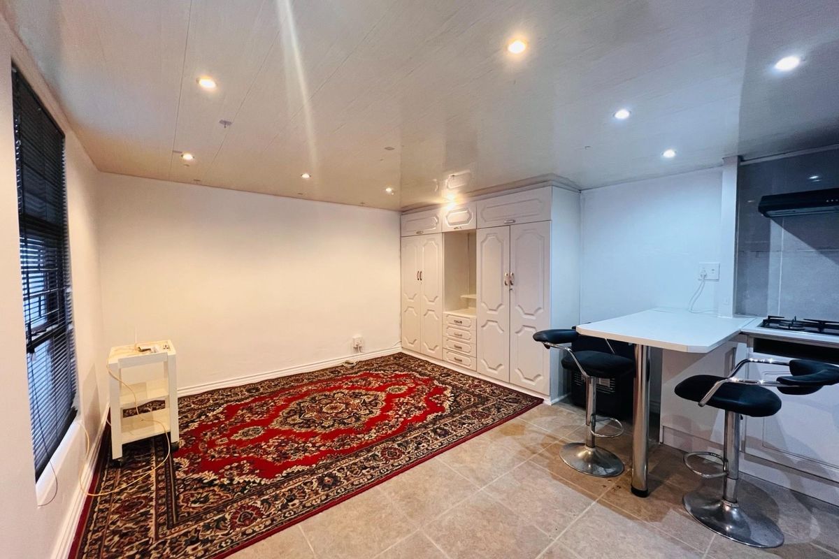 Open-plan living area featuring tiled floors, recessed lighting, built-in storage cupboards, and a compact kitchen breakfast counter with integrated hob and extractor.