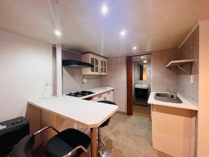 Compact kitchen featuring built-in cabinetry, gas hob, extractor fan, and a breakfast counter, with direct access to an adjoining bathroom.