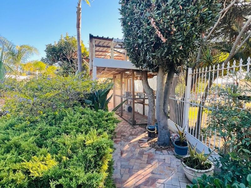 A well-maintained garden path featuring brick paving, mature trees, and a secure metal perimeter fence, providing a pleasant outdoor walkway.