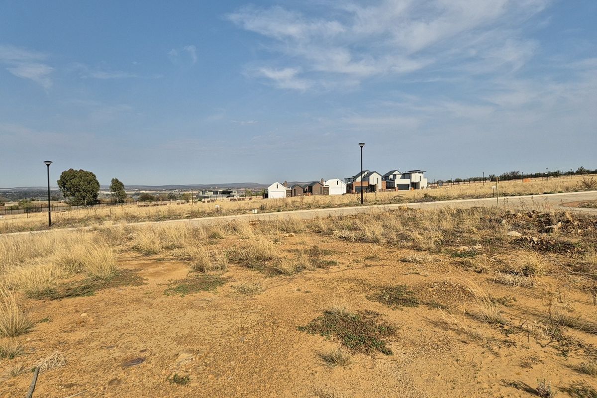 A view of a vacant residential plot featuring a paved road and street lighting, with neighboring houses visible in the distance.