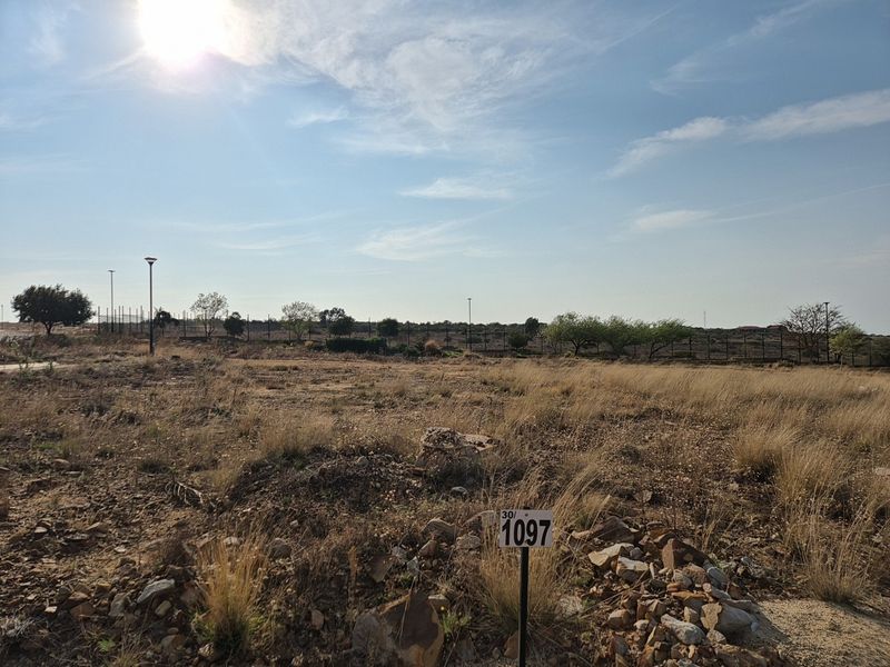 A vacant residential plot featuring natural vegetation, perimeter fencing, and street lighting, ready for development.