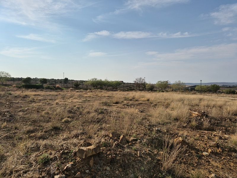 A vacant residential plot featuring natural dry grass, rocky terrain, and perimeter fencing, offering a clear space for future development.