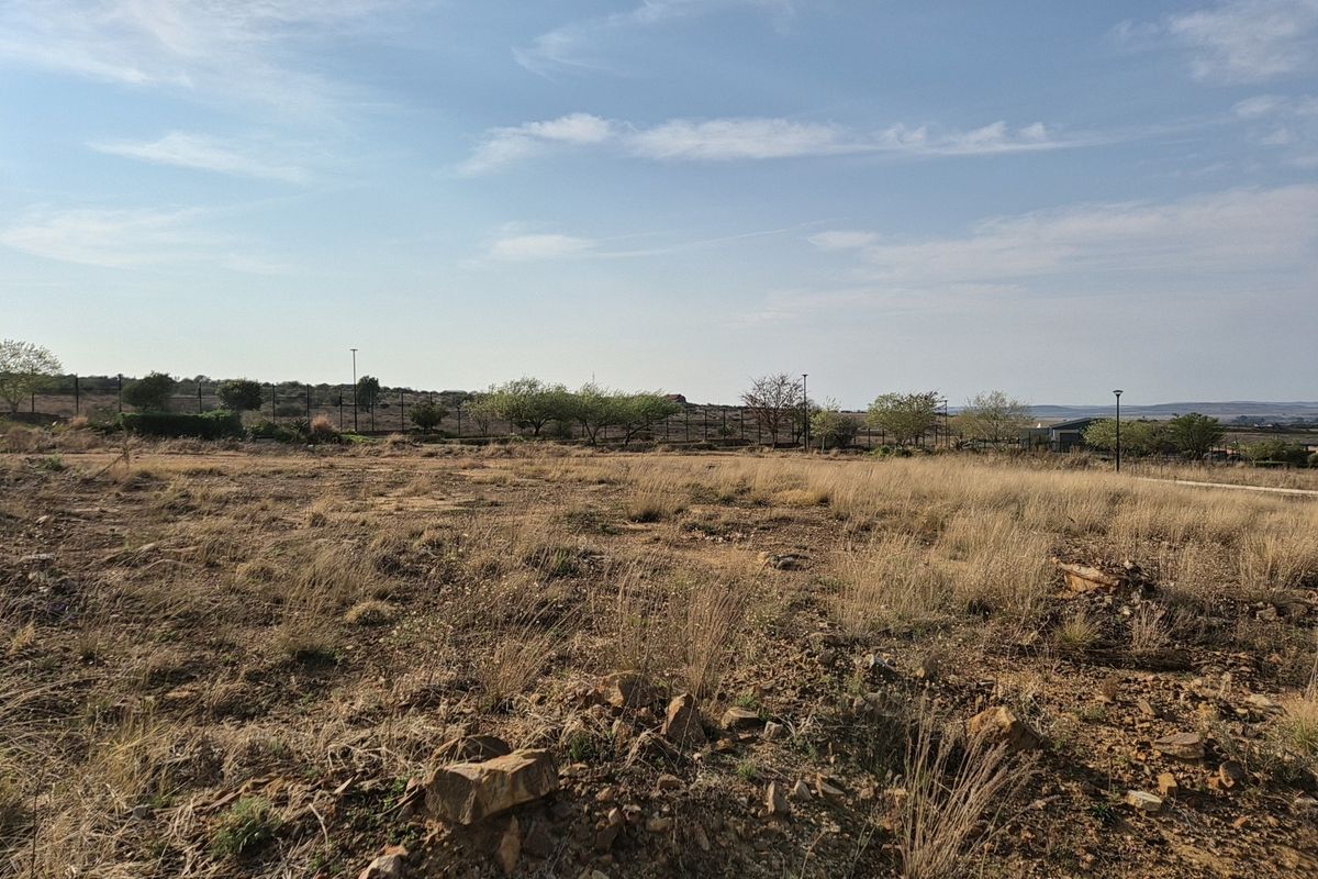 A vacant residential plot featuring natural dry grass, rocky terrain, and perimeter fencing, offering a clear space for future development.