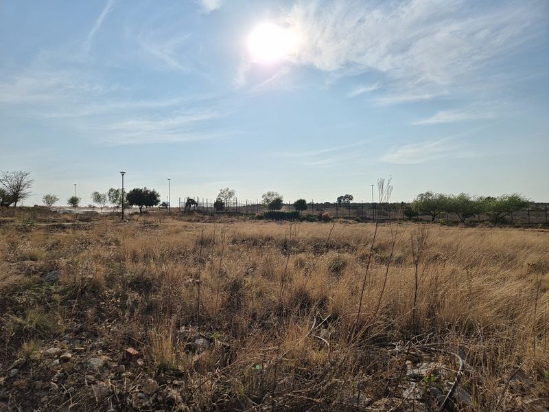 A view of a vacant residential plot featuring dry grass, perimeter fencing, and street lighting under a clear sky.