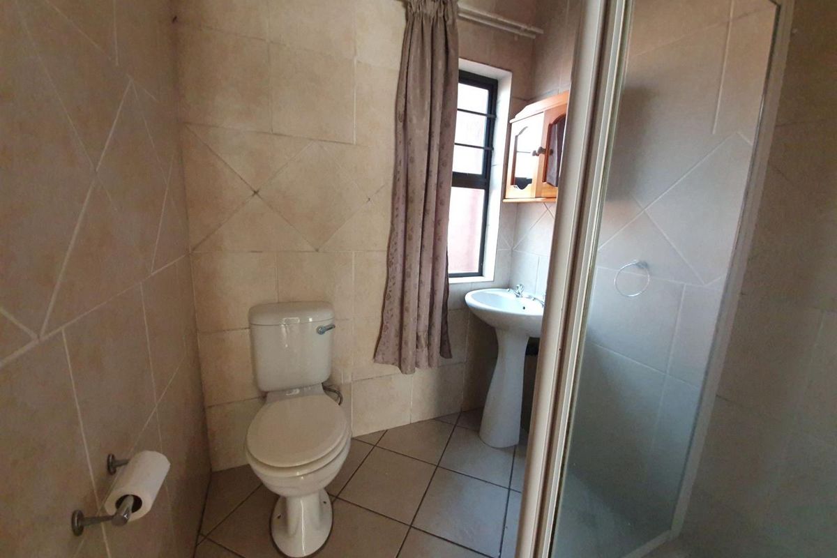 A functional bathroom featuring a pedestal basin, toilet, and shower enclosure with neutral wall and floor tiling.