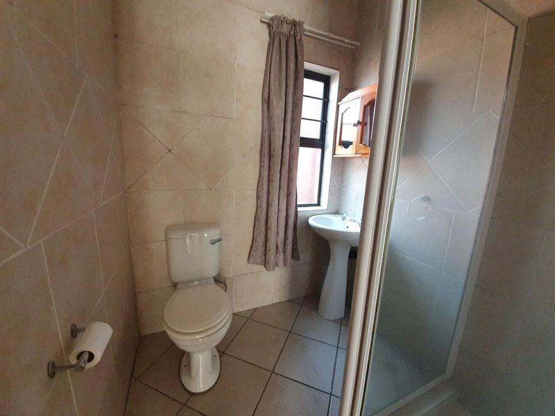 A functional bathroom featuring a pedestal basin, toilet, and shower enclosure with neutral wall and floor tiling.