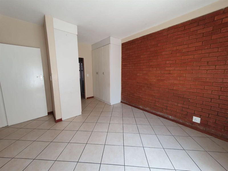 A vacant bedroom featuring a distinctive exposed brick wall, neutral ceramic floor tiles, and built-in storage cupboards.