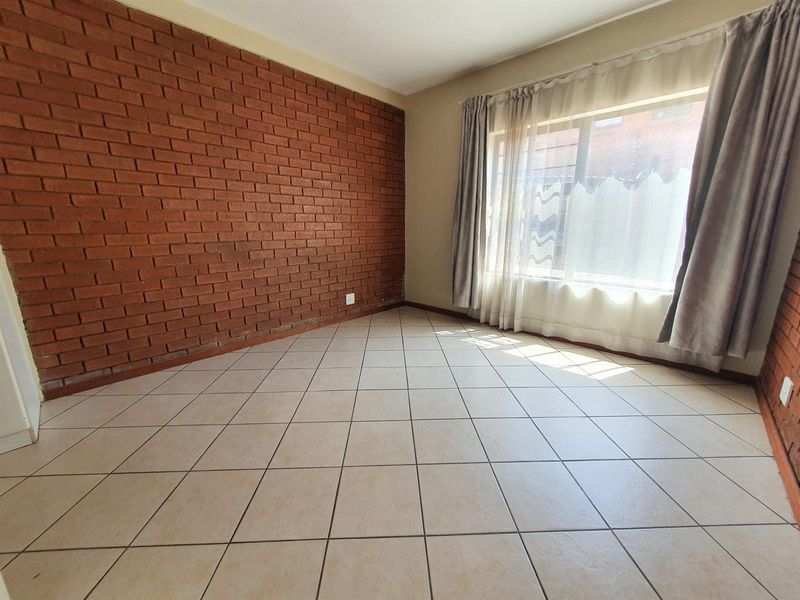 A bright, empty bedroom featuring a distinctive exposed brick wall and neutral ceramic floor tiles, offering a versatile space ready for personalization.