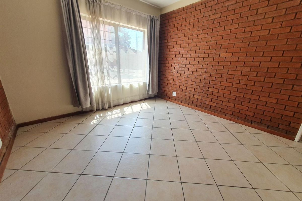 A bright, empty bedroom featuring a distinctive exposed brick feature wall and neutral ceramic floor tiles, offering a clean canvas for personalization.