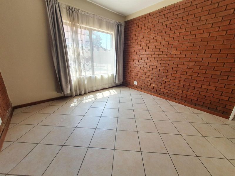 A bright, empty bedroom featuring a distinctive exposed brick feature wall and neutral ceramic floor tiles, offering a clean canvas for personalization.