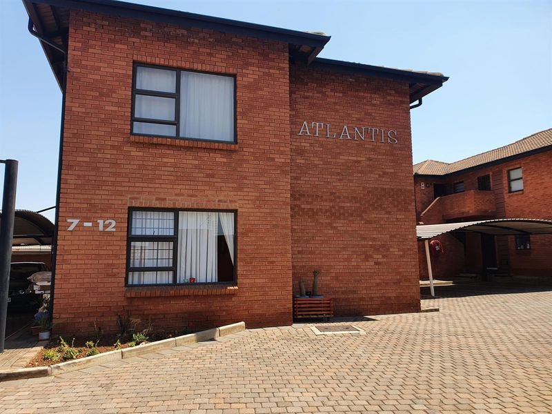 Exterior view of the Atlantis townhouse complex featuring face brick construction, paved driveway, and covered carport parking.