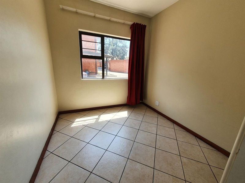 A vacant bedroom featuring neutral wall paint, tiled flooring, and an aluminium window frame, offering a blank canvas for personalization.