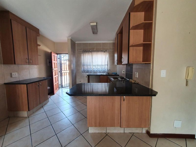 A functional kitchen featuring wooden cabinetry, granite countertops, a built-in gas hob, and tiled flooring with direct access to an exterior door.