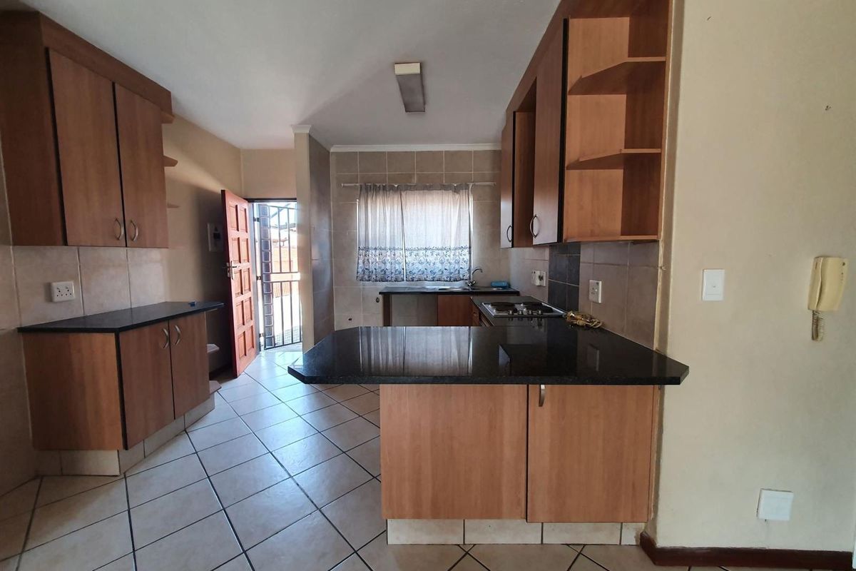 A functional kitchen featuring wooden cabinetry, granite countertops, a built-in gas hob, and tiled flooring with direct access to an exterior door.