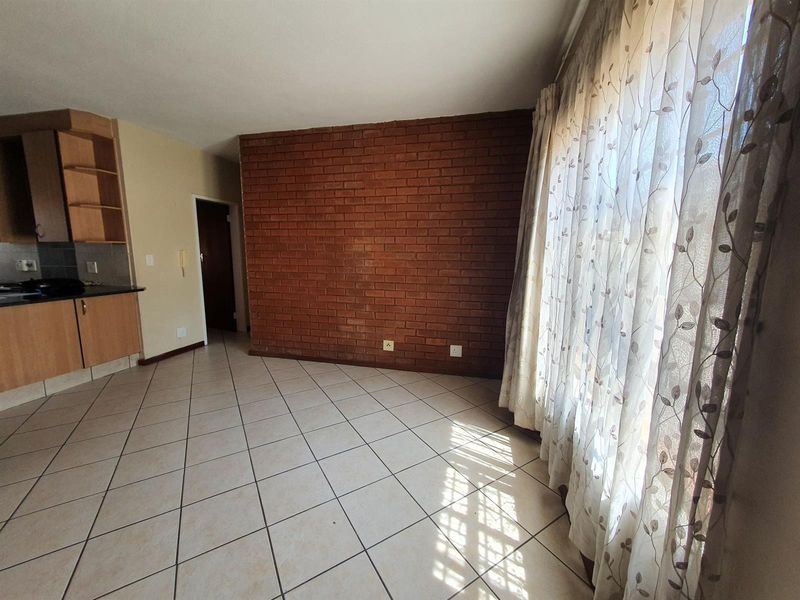 Open plan living area featuring an exposed brick accent wall, ceramic tiled flooring, and an adjacent kitchen with built-in cabinetry.