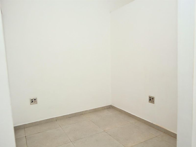An empty, neutral-toned room featuring tiled flooring and wall-mounted electrical outlets, suitable for use as a bedroom or home office.