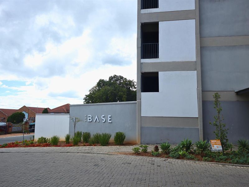 Front exterior view of The Base apartment complex featuring paved driveway access, modern building facade, and landscaped garden beds.