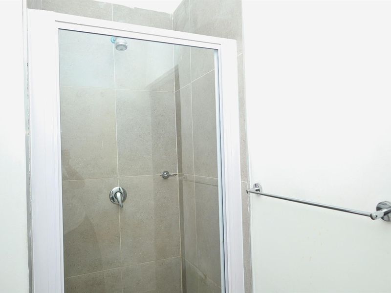 A clean bathroom shower area featuring a glass enclosure, modern shower mixer, and a wall-mounted towel rail with neutral wall tiling.
