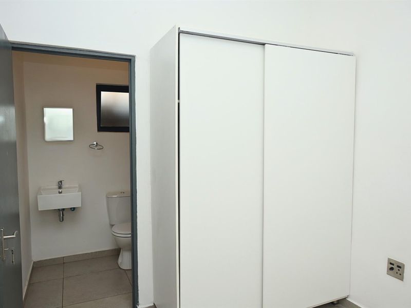 A clean bedroom featuring a built-in sliding door wardrobe and direct access to an en-suite bathroom with a wall-mounted basin and toilet.