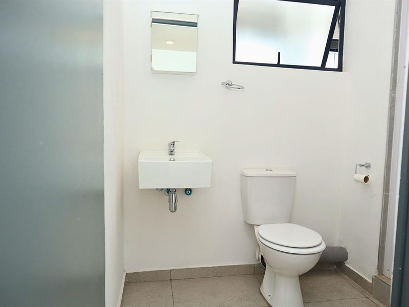A functional, compact bathroom featuring a wall-mounted basin, standard toilet, and tiled flooring with a top-hung window for ventilation.