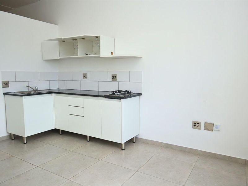 A compact, empty kitchen featuring white cabinetry, a dark stone countertop, a gas hob, and tiled splashbacks, ready for personalization.