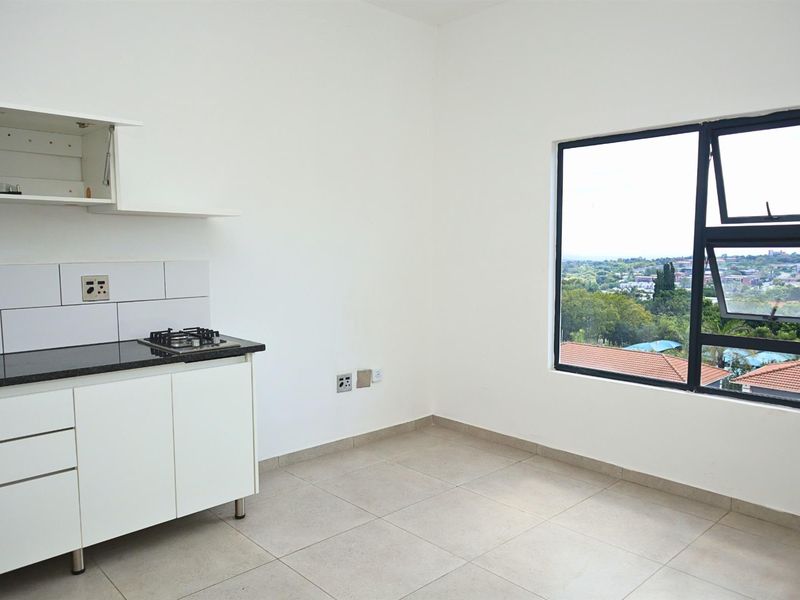 A clean, modern kitchen area featuring white cabinetry, granite countertops, a gas hob, and large windows offering an elevated view.