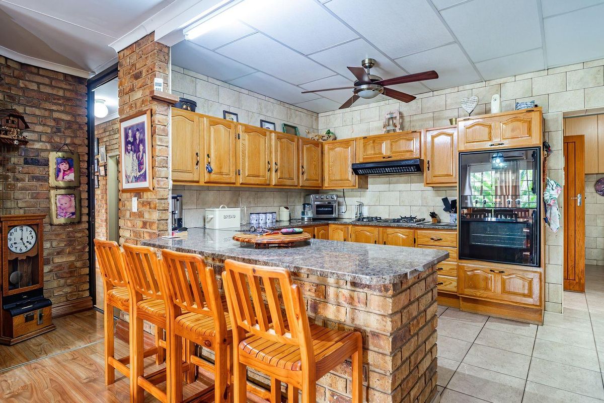 A traditional kitchen featuring exposed brick accents, granite countertops, a breakfast bar, and built-in appliances with wooden cabinetry.