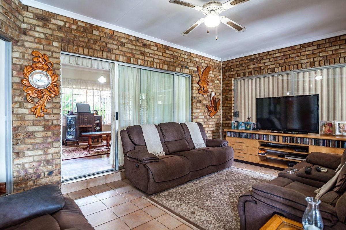 A living room featuring exposed brick walls, tiled flooring, and a ceiling fan, with sliding glass doors providing access to an adjacent room.