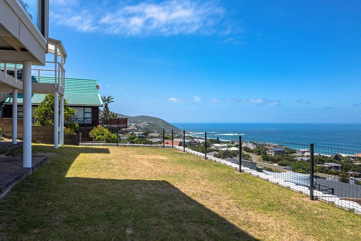A spacious rear garden area featuring a manicured lawn, wire mesh fencing, and expansive coastal views overlooking the surrounding neighborhood and ocean.