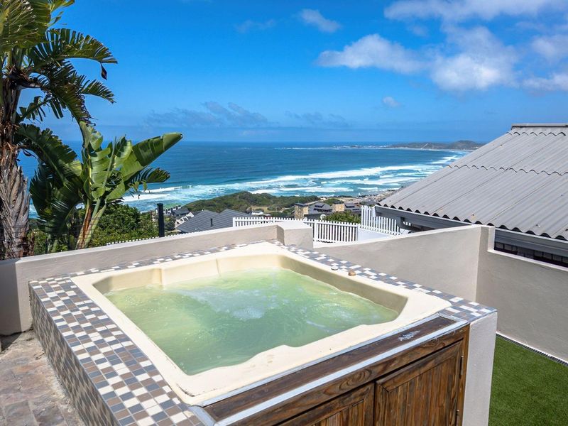 An elevated outdoor deck featuring a built-in spa pool with panoramic ocean and coastal views.