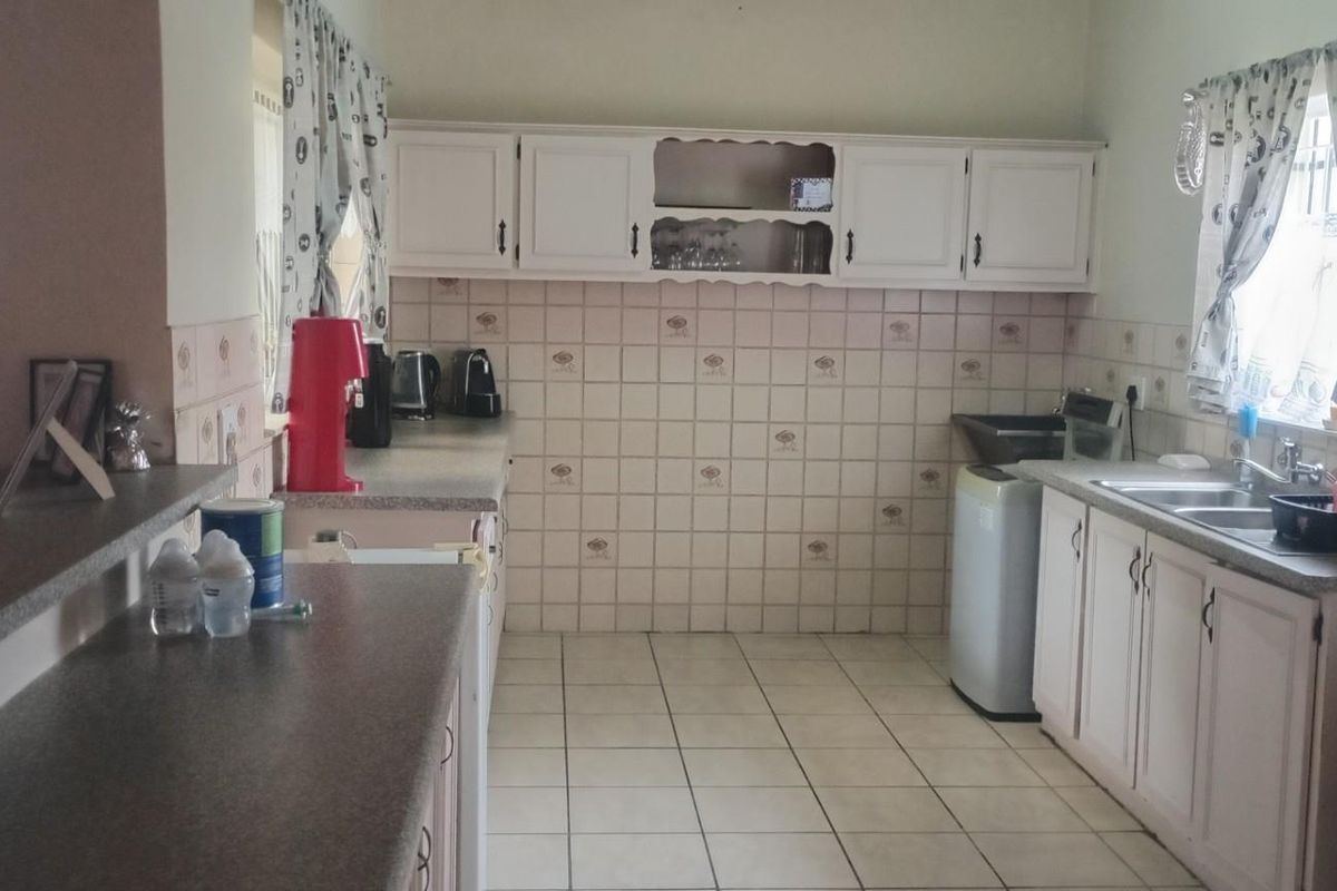A functional kitchen featuring white cabinetry, tiled backsplash, laminate countertops, and a double basin sink with tiled flooring.