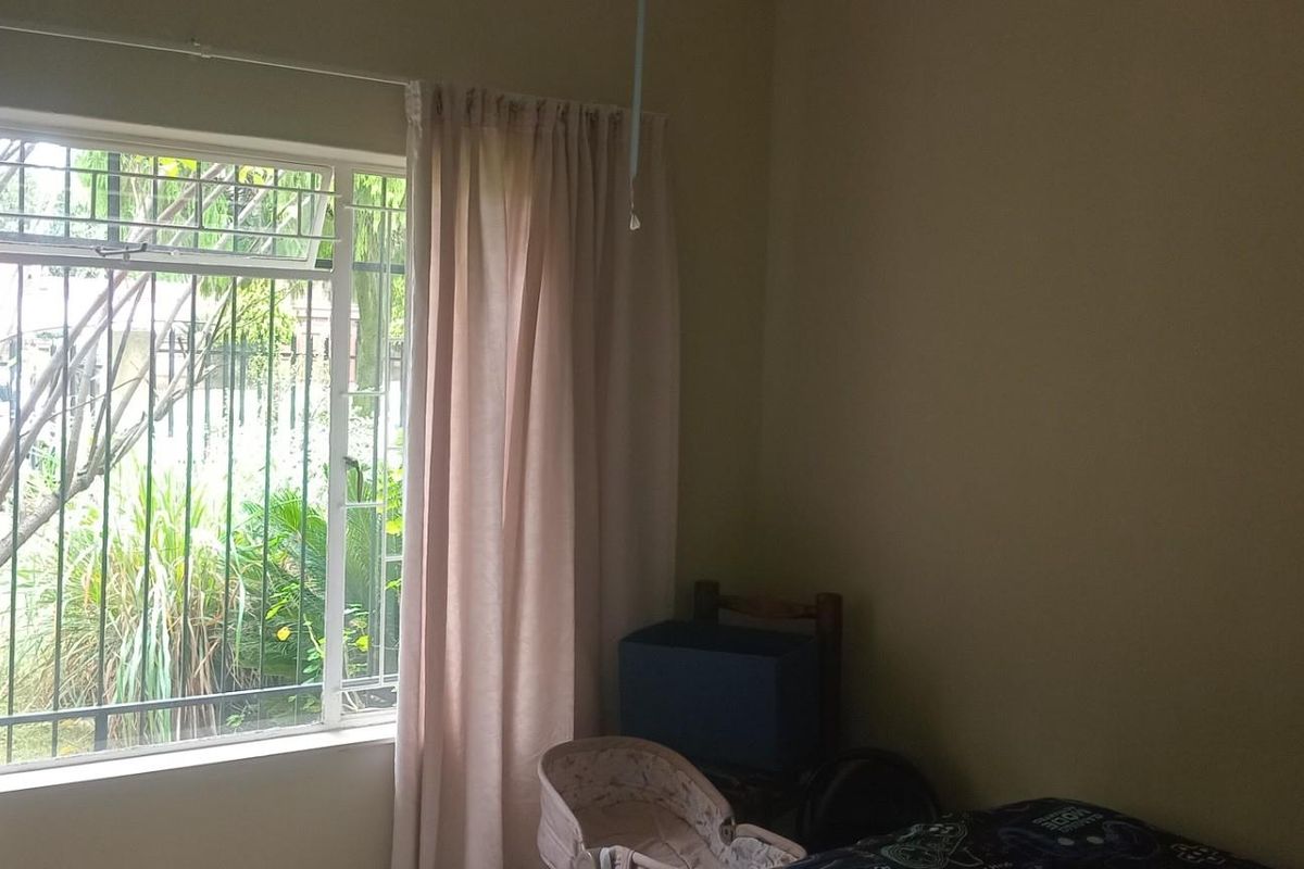 A bedroom featuring a window with security bars and curtains, providing natural light and a view of the garden area.
