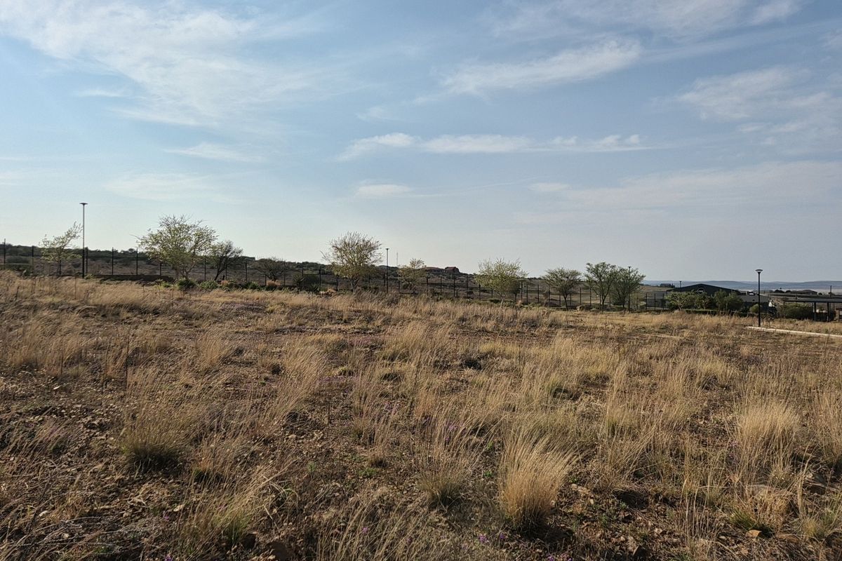 A vacant residential plot featuring natural dry grass, perimeter fencing, and established trees, offering a blank canvas for future development.