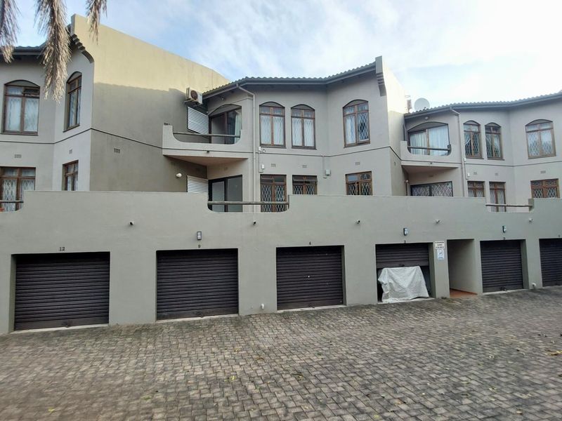 Exterior view of an apartment complex featuring multiple ground-level garage units and upper-level residential units with arched windows and balconies.