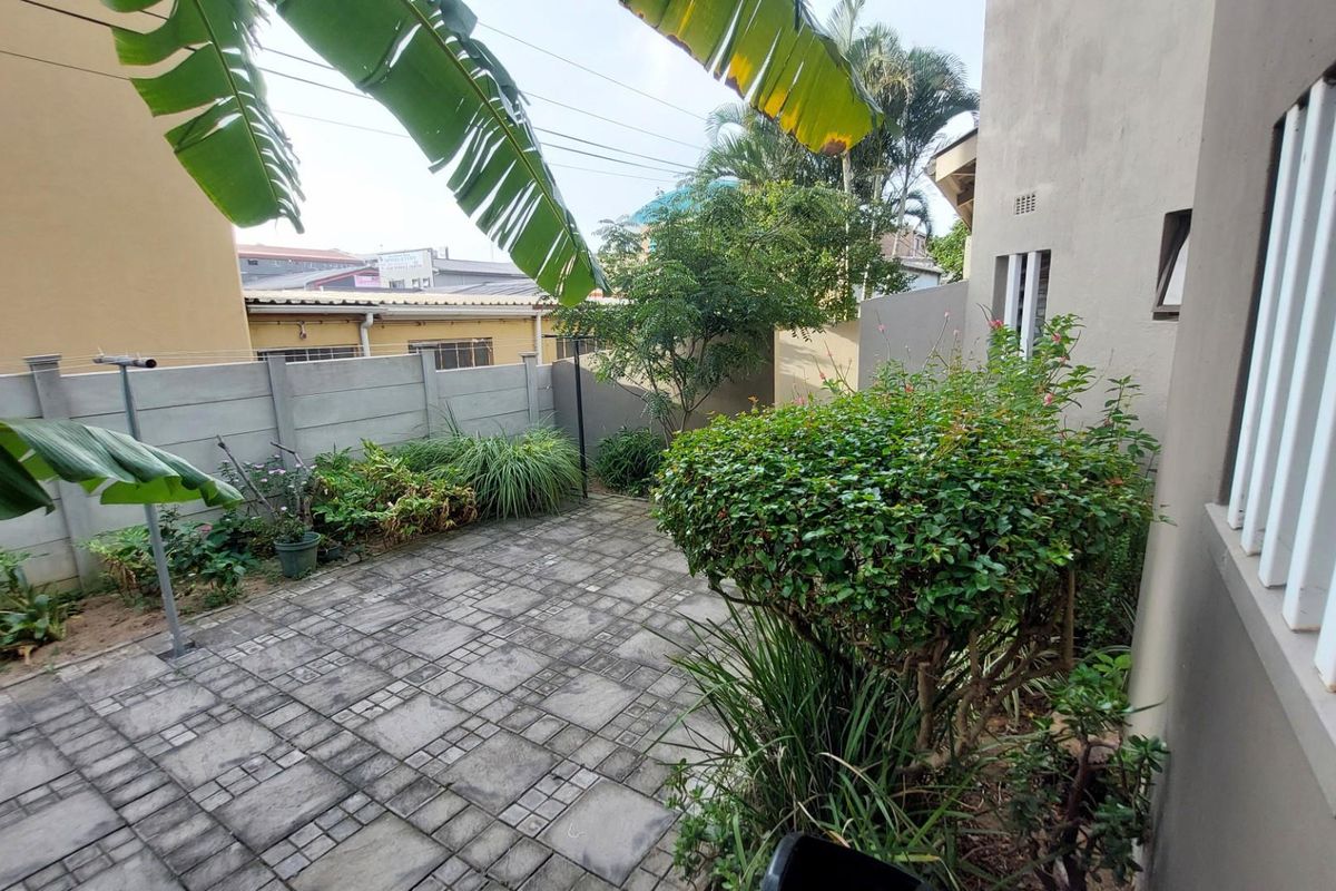 A private rear courtyard featuring paved flooring, perimeter boundary walls, and established garden landscaping.