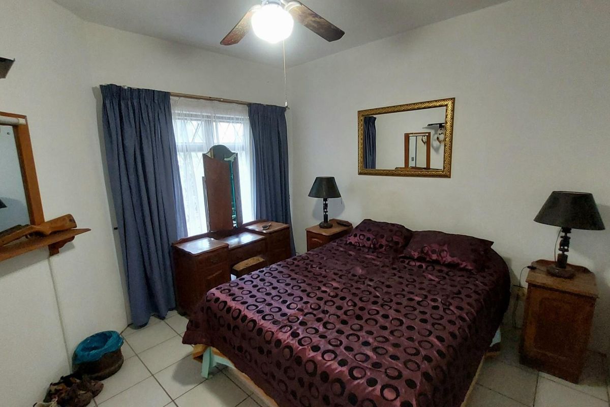 A bedroom featuring tiled flooring, a ceiling fan, and a window with curtains.