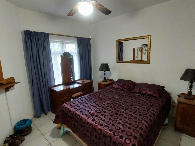 A bedroom featuring tiled flooring, a ceiling fan, and a window with curtains.