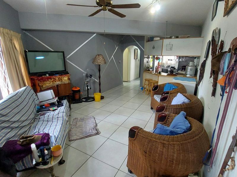 Open plan living area featuring tiled flooring, a ceiling fan, and a breakfast bar connecting to the kitchen space.