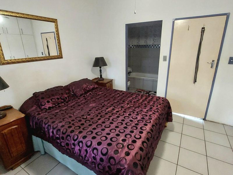 A bedroom featuring tiled flooring, built-in cupboards, and an en-suite bathroom with a bathtub.