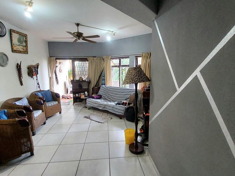 A spacious living area featuring tiled flooring, a ceiling fan, and large windows providing natural light, with direct access to an outdoor patio space.