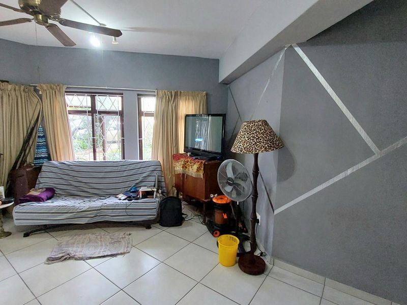 A living room featuring tiled flooring, a ceiling fan, and a decorative painted accent wall with large windows providing natural light.