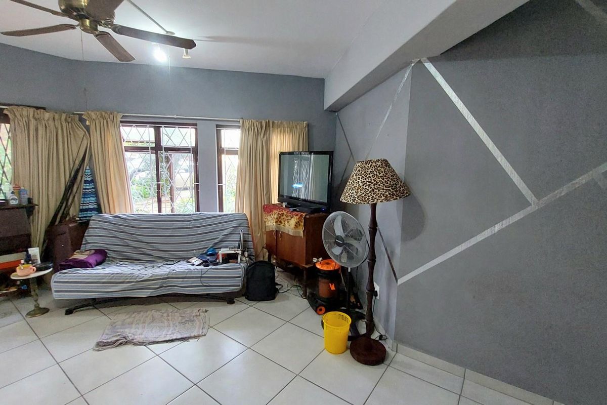 A living room featuring tiled flooring, a ceiling fan, and a decorative painted accent wall with large windows providing natural light.