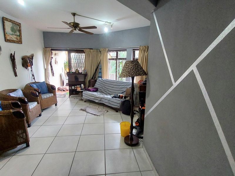 Spacious living area featuring tiled flooring, a ceiling fan, and large windows providing natural light, with direct access to an outdoor patio space.