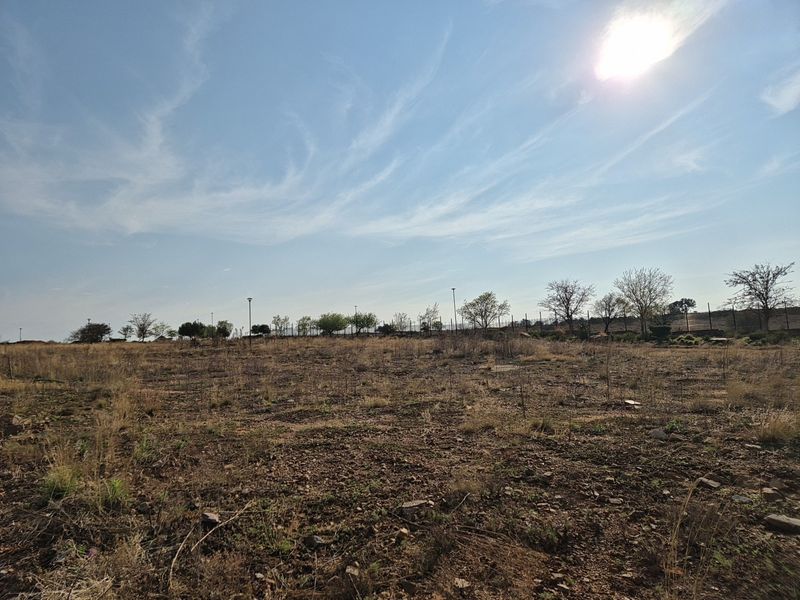 A wide-angle view of a vacant residential plot featuring natural terrain and perimeter fencing under a clear sky.