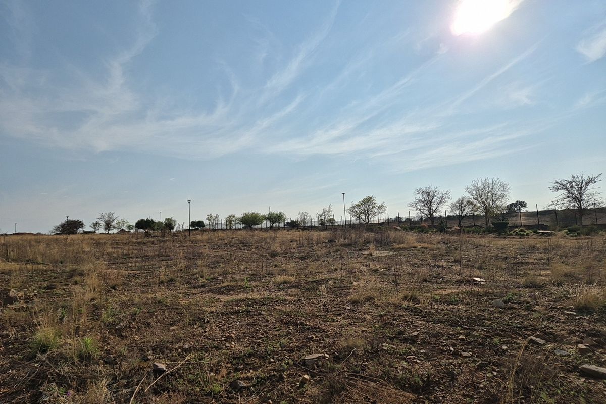 A wide-angle view of a vacant residential plot featuring natural terrain and perimeter fencing under a clear sky.