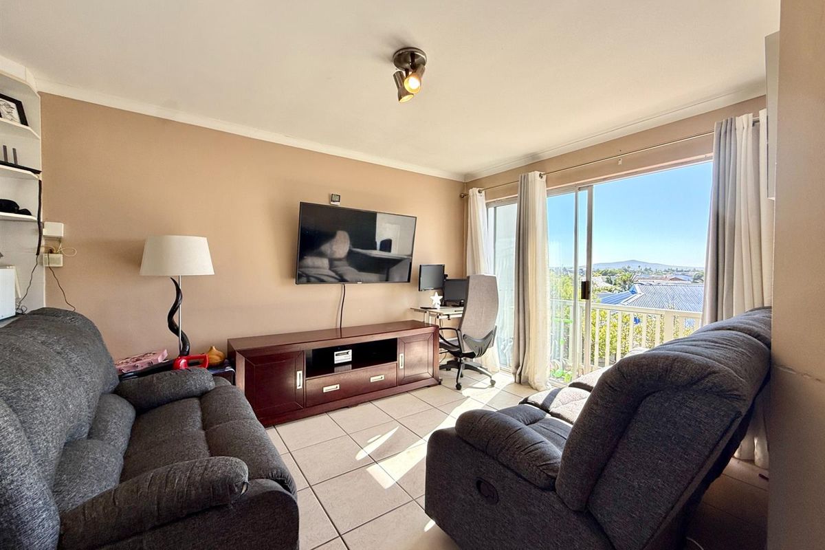A bright living room featuring tiled flooring and large sliding glass doors that open onto a balcony with scenic views.