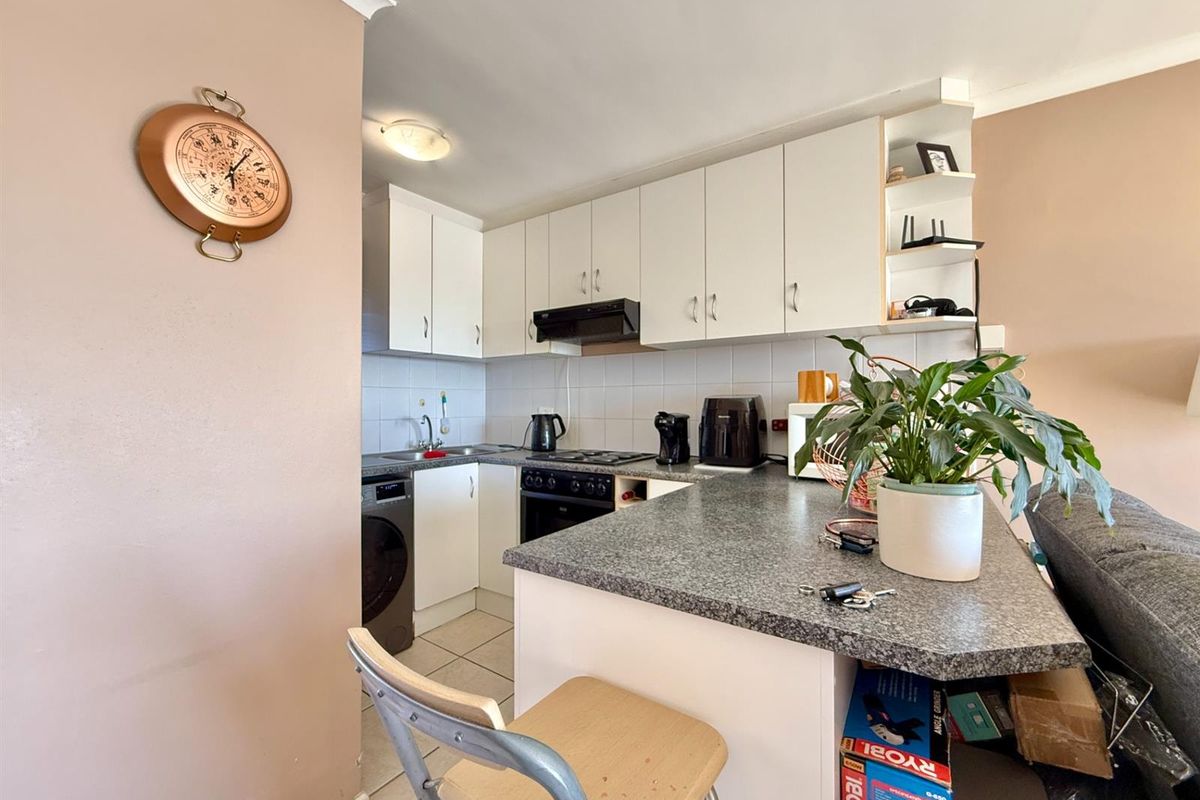 Compact kitchen featuring white cabinetry, laminate countertops, tiled backsplash, and integrated stove with extractor fan, designed for efficient apartment living.
